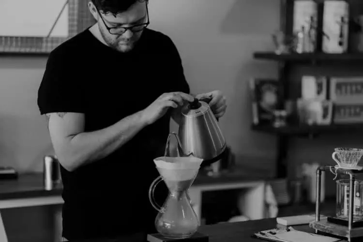Man pouring hot water in a carafe with a white coffee filter
